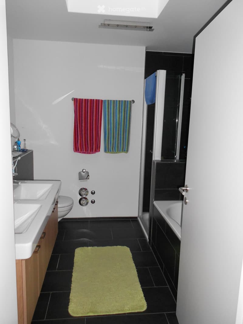 Modern bathroom with white walls, black tiles, a sink, toilet, bathtub, and colorful towels.