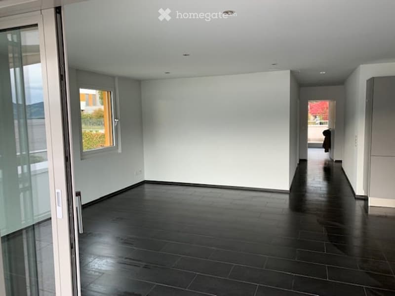 Empty room with dark tiled floor, white walls, large window, and glass door leading to balcony.