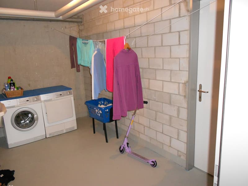 Laundry room with washing machine, dryer, clothes hanging on a line, a scooter, and a laundry basket.