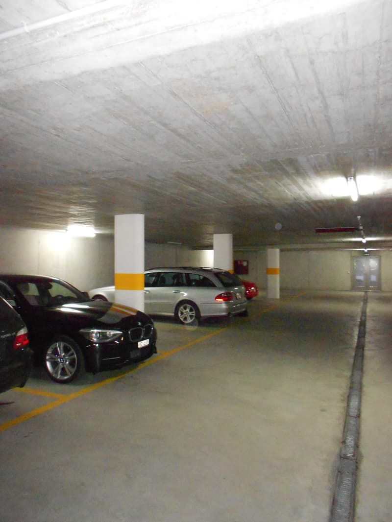 Underground parking area with several parked cars, concrete pillars, and yellow parking lines.