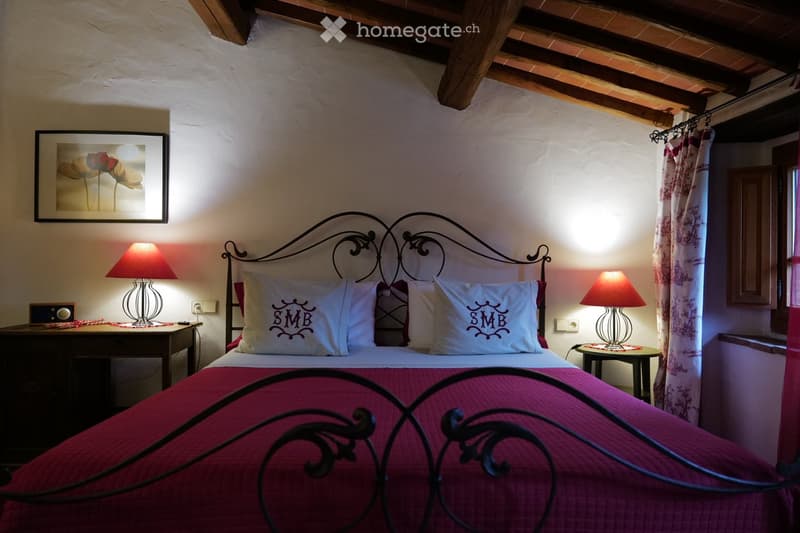 Cozy bedroom with a wrought iron bed, red bedding, two nightstands with lamps, and a framed picture on the wall.