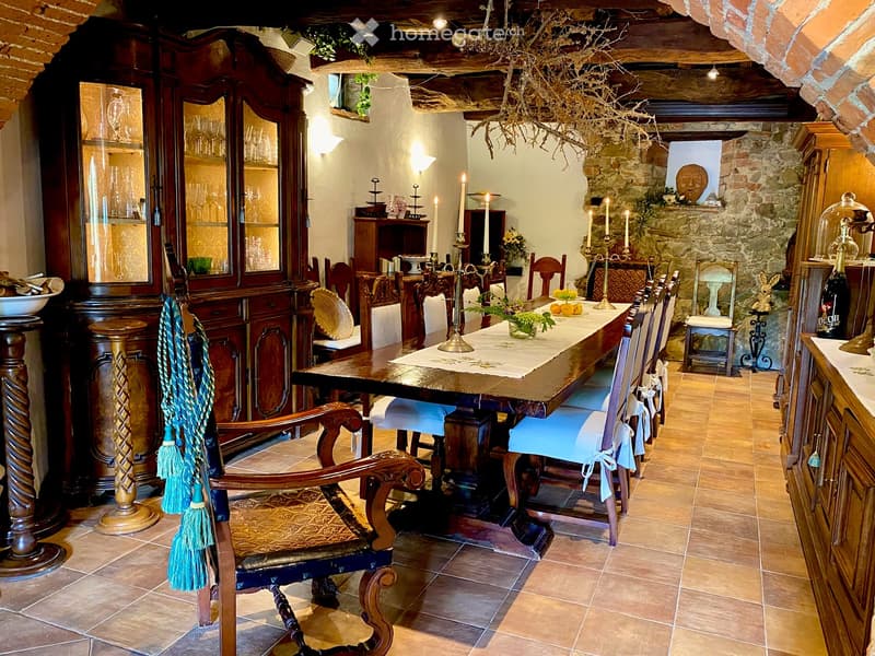 Elegant dining room with a long wooden table set with chairs, a chandelier, and decorative items including candles and a vase.