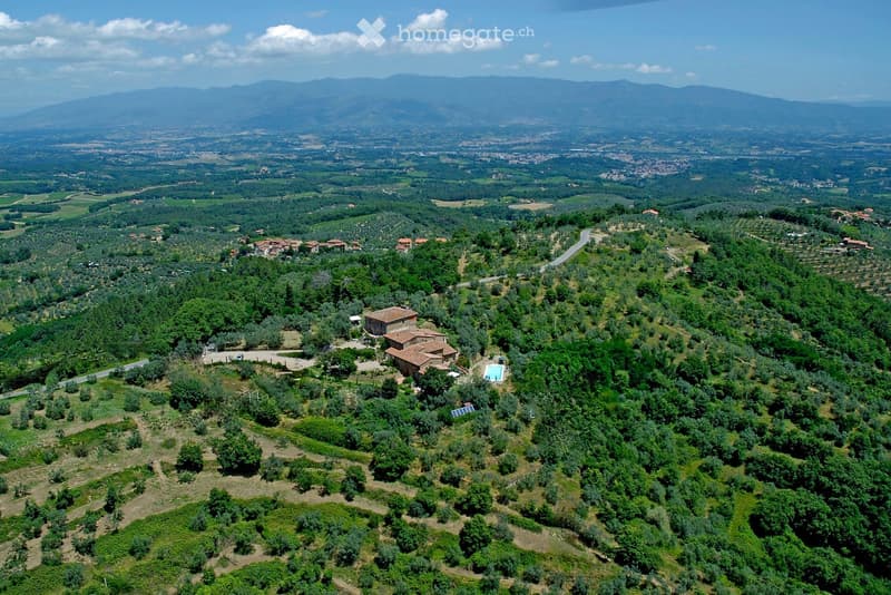 Aerial view of a rural estate with a house, swimming pool, olive groves, and surrounding hills and mountains.