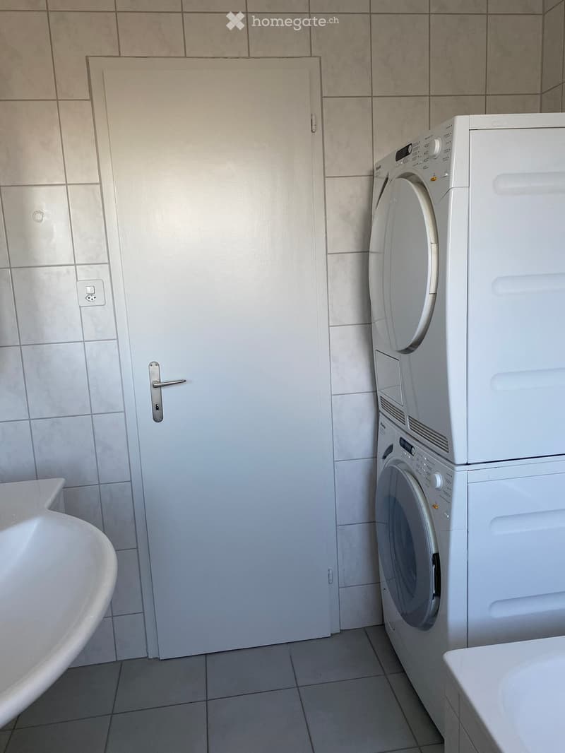 Bathroom with a bathtub, a washing machine, and a door.