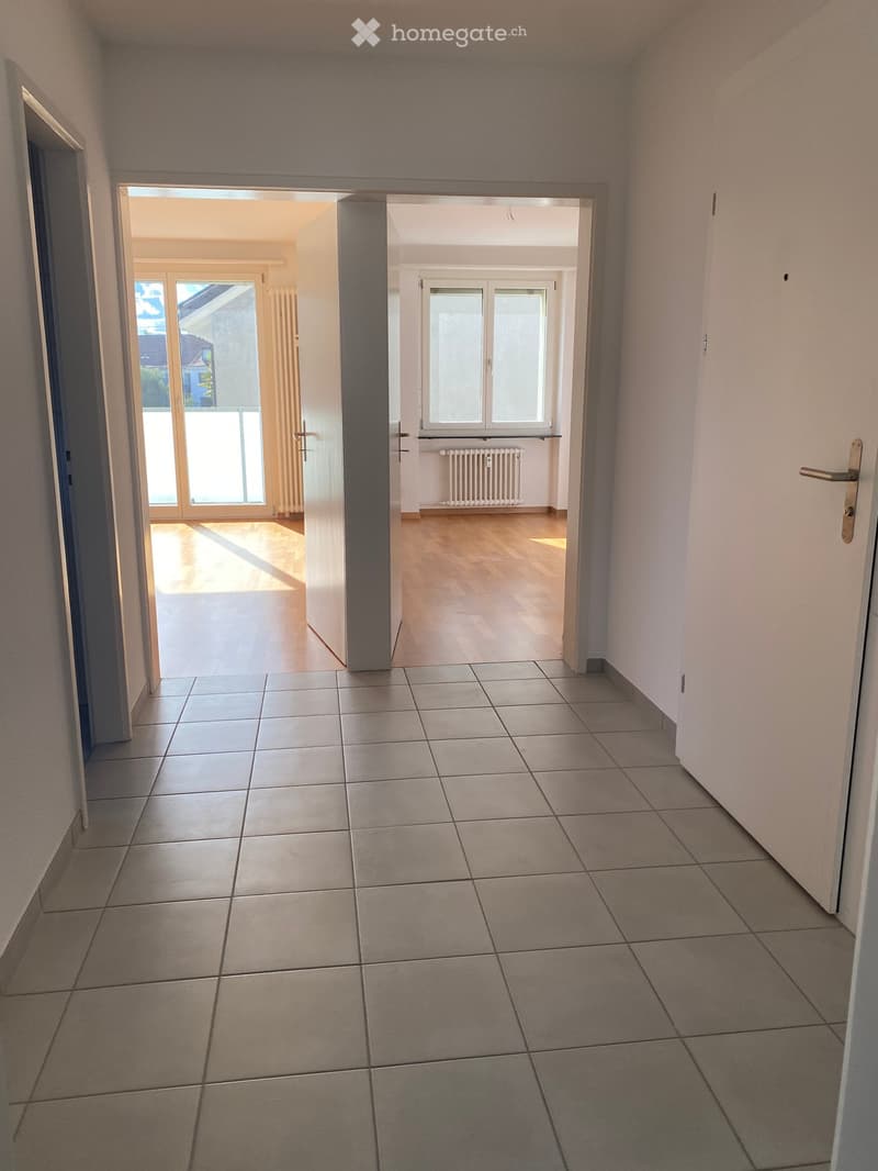Empty hallway with tiled floor, white walls, and doors leading to other rooms. Natural light from adjacent rooms.