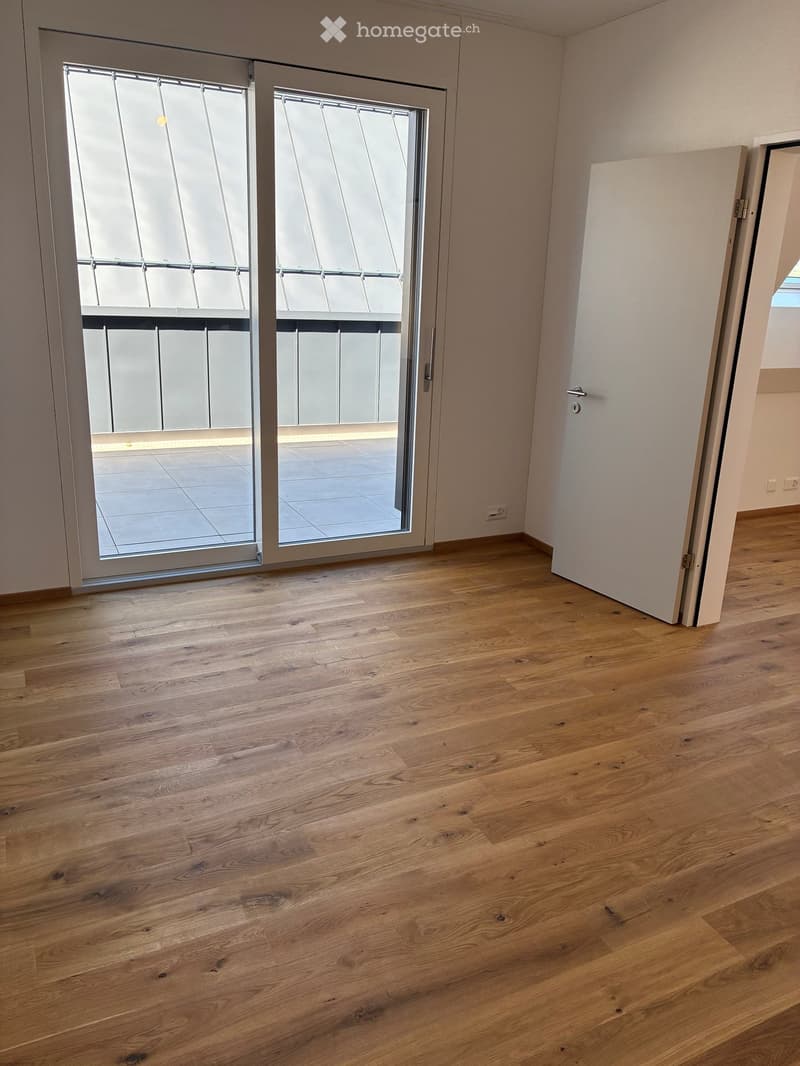 Empty room with wooden flooring, large sliding glass doors leading to a balcony, and white walls.