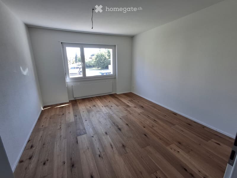 Empty room with wooden flooring, white walls, and a large window with a radiator below it.