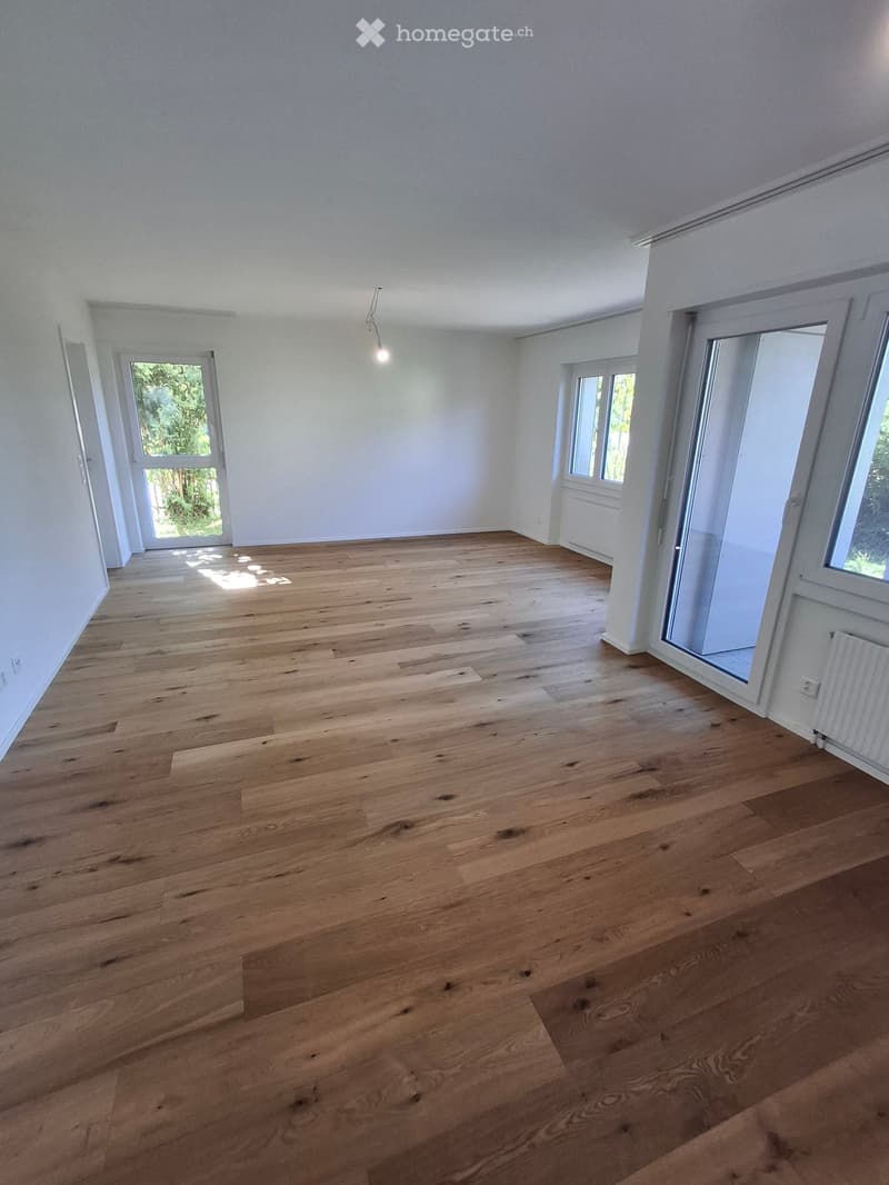 Empty room with wooden flooring, white walls, and large windows allowing natural light. No furniture or equipment is present.