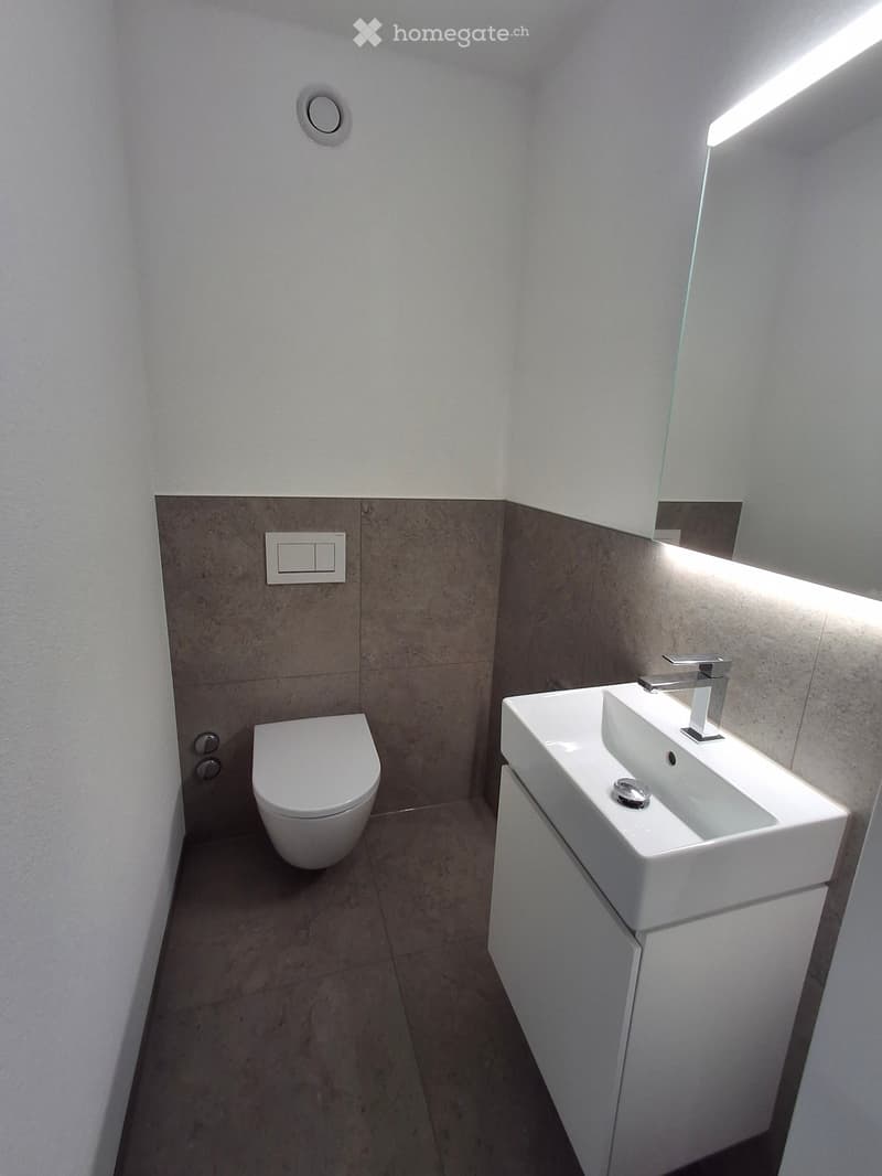 Modern bathroom with a toilet, sink, and faucet. The walls are tiled in a two-tone design, and the floor is tiled in a neutral tone.