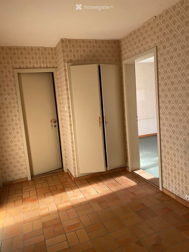 Empty room with patterned wallpaper, tiled floor, and two doors, one leading to an open space.