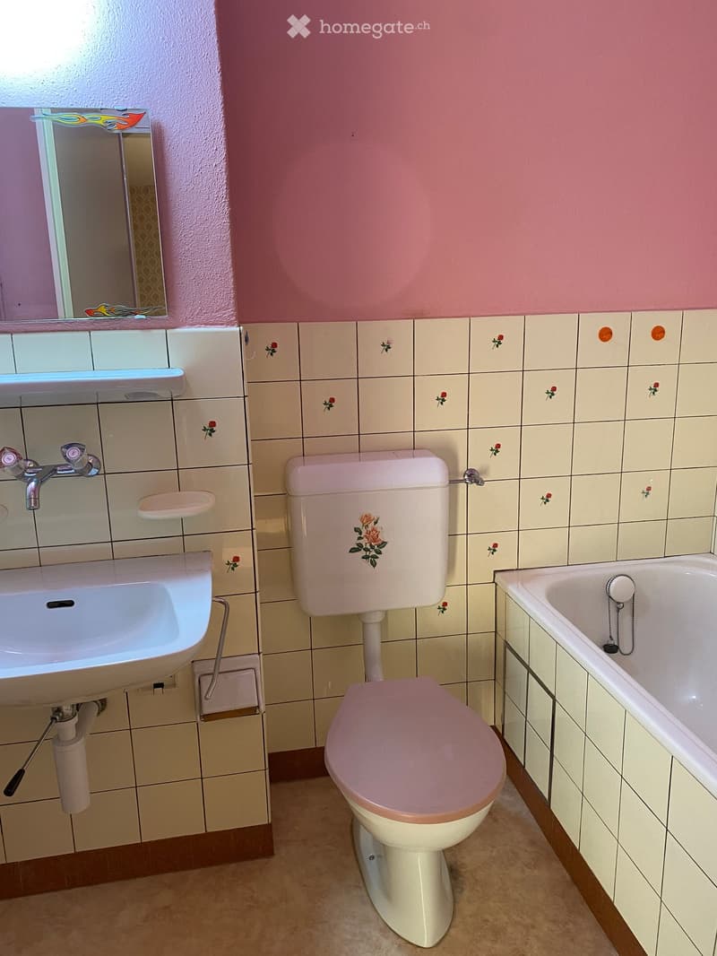 Bathroom with pink walls, tiled walls with floral designs, a white sink, a toilet, and a bathtub.
