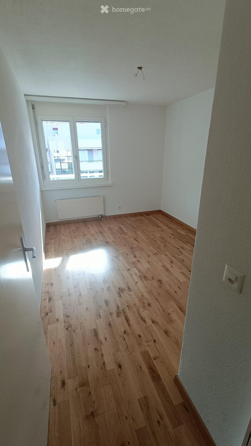 Empty room with wooden flooring, white walls, and a window with a view of the outside. No furniture or equipment is present.