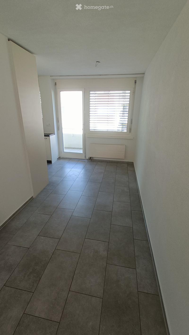 Empty hallway with tiled floor, white walls, a window with blinds, and a door leading to another room.