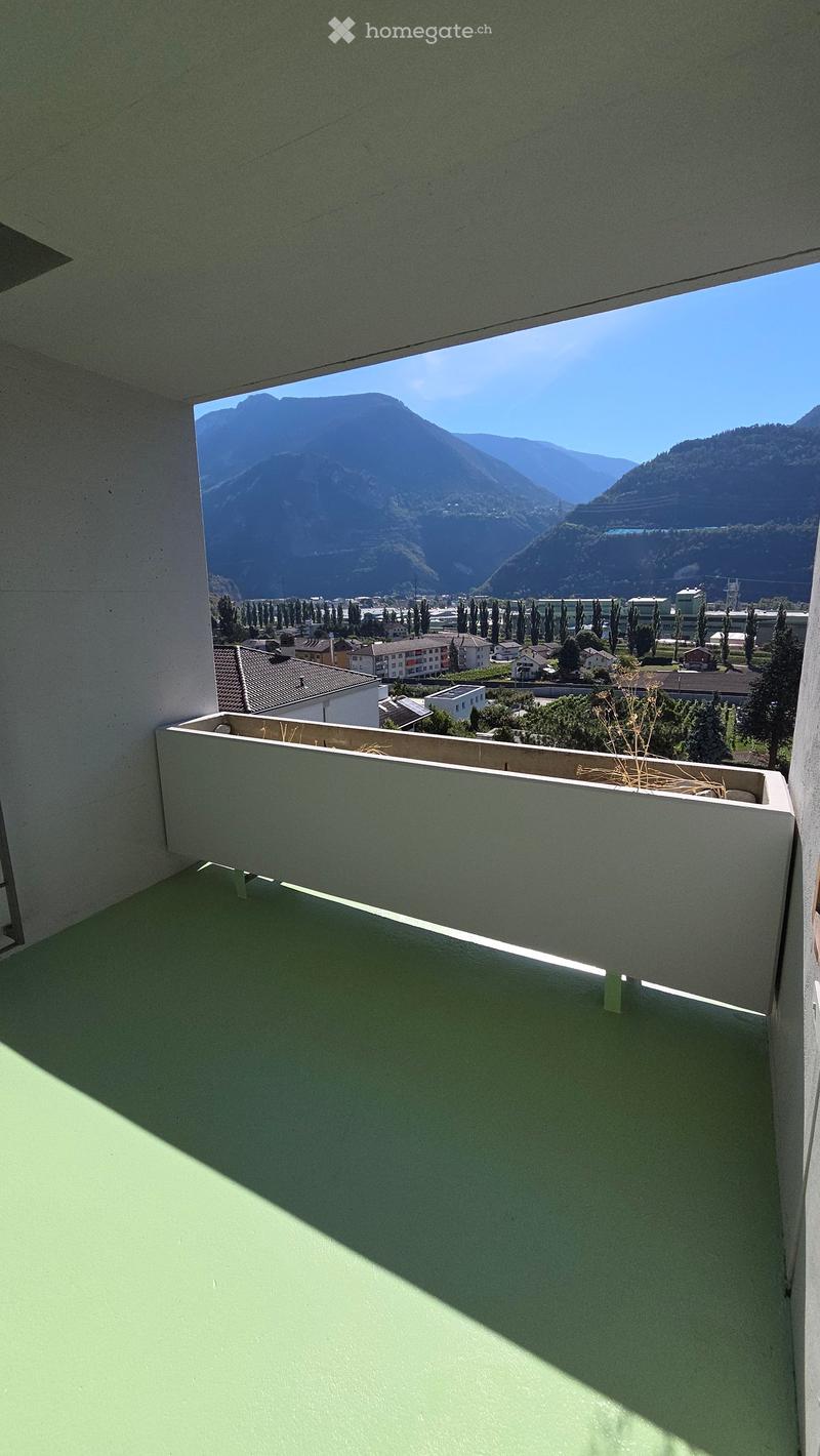 Balcony with a green floor and white railing, overlooking a town and mountain landscape.