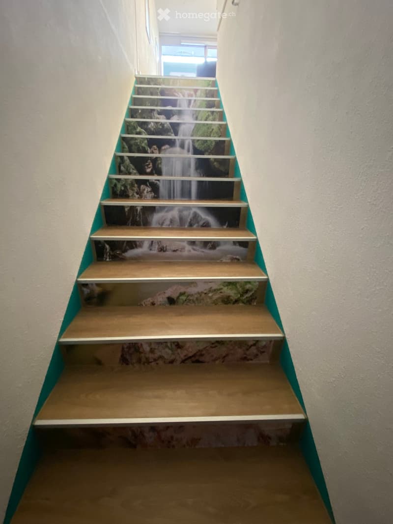 Wooden staircase with a waterfall mural design on the risers, light-colored walls, and a window at the top of the stairs.