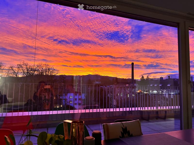 Balcony with a view of a sunset, featuring a table, chairs, and a cup on the table.