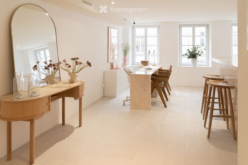Modern, minimalist room with a vanity table, a large mirror, a marble dining table with chairs, and wooden stools near a window.