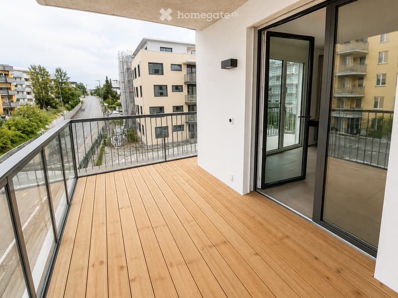 Balcony with wooden decking, glass railing, and sliding glass door leading to interior.