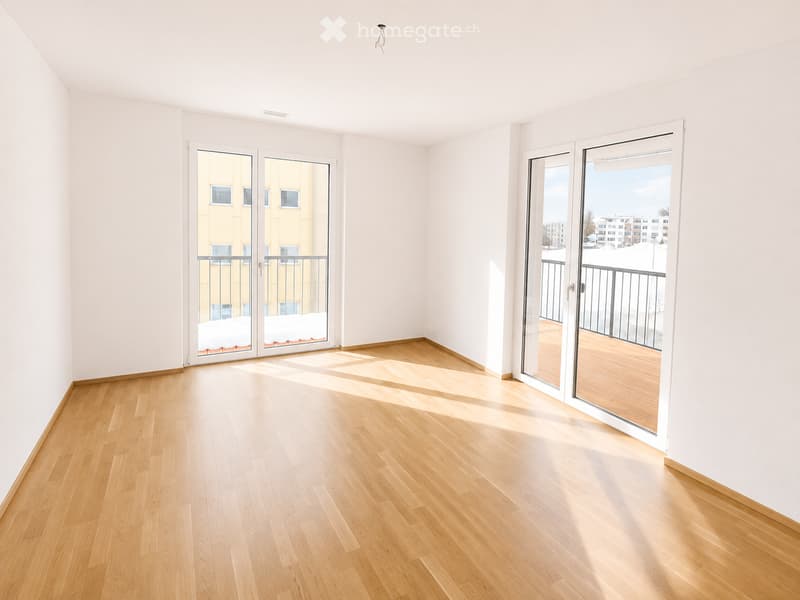 Empty room with light wooden flooring and white walls, featuring two sets of sliding glass doors leading to balconies.
