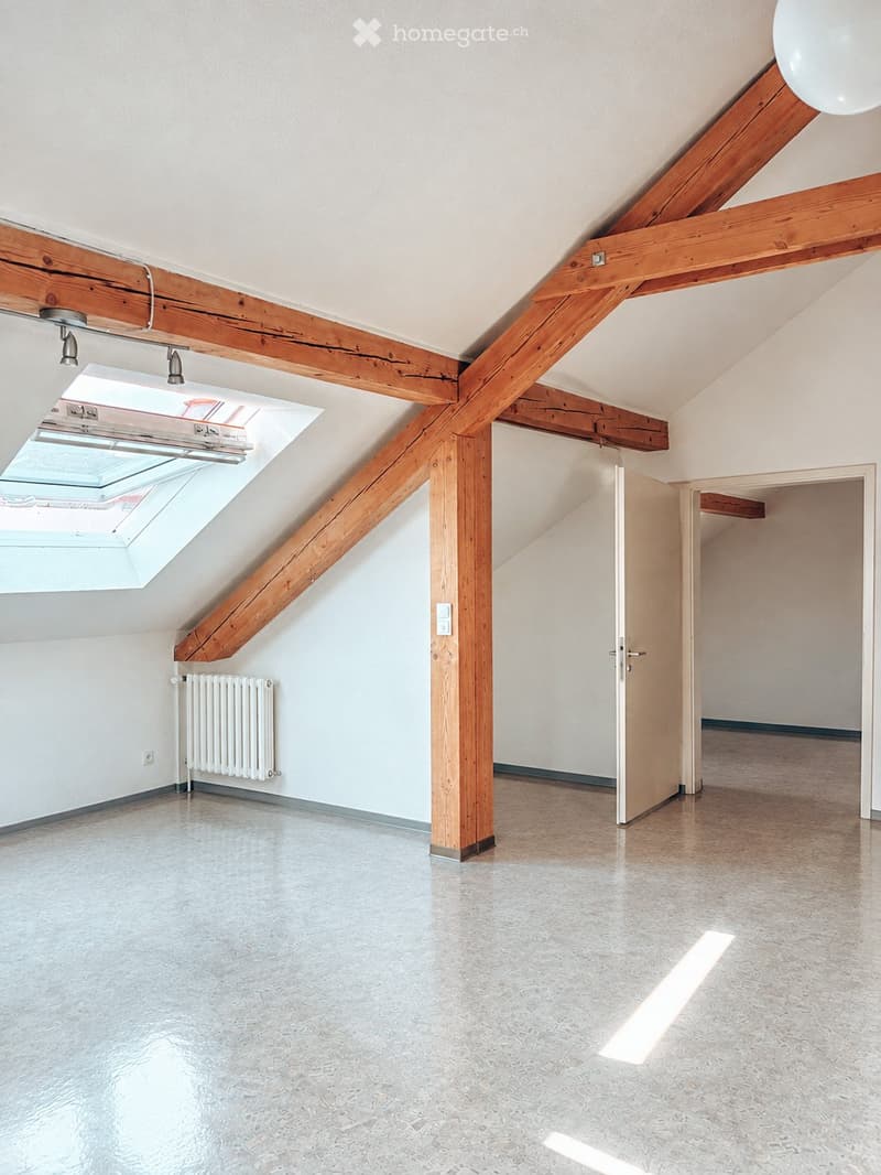 Empty attic space with exposed wooden beams, skylight window, radiator, and modern flooring.