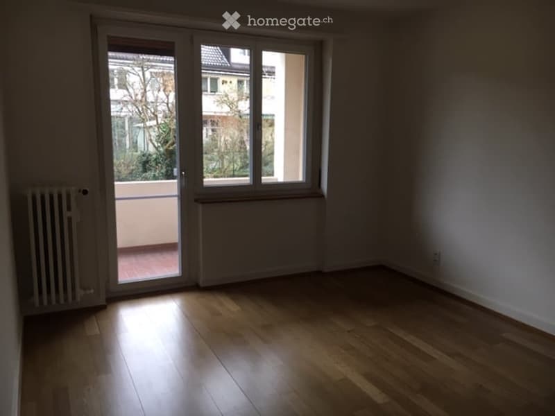Empty room with wooden flooring, large window, and sliding glass door leading to a balcony.