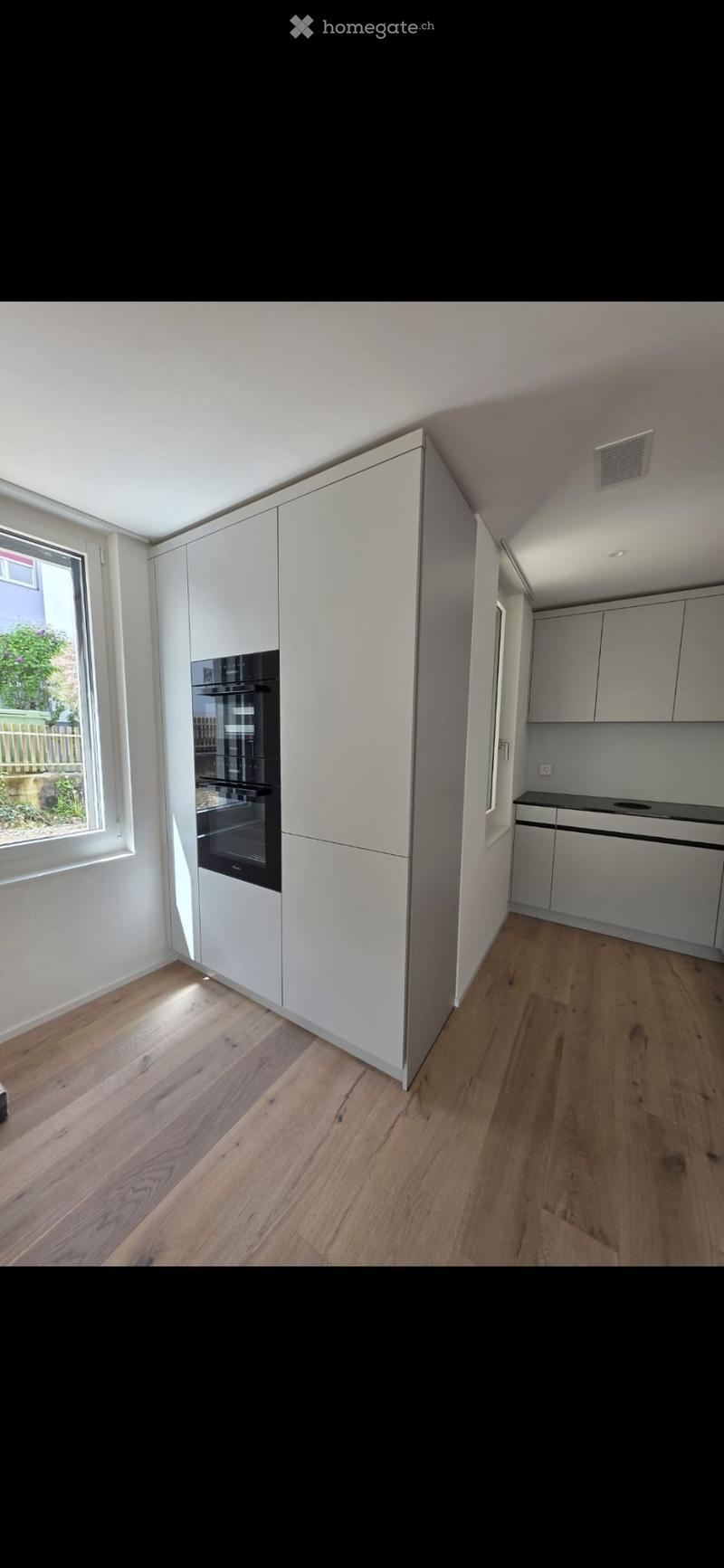 Modern kitchen with white cabinets, a built-in oven, and wooden flooring.