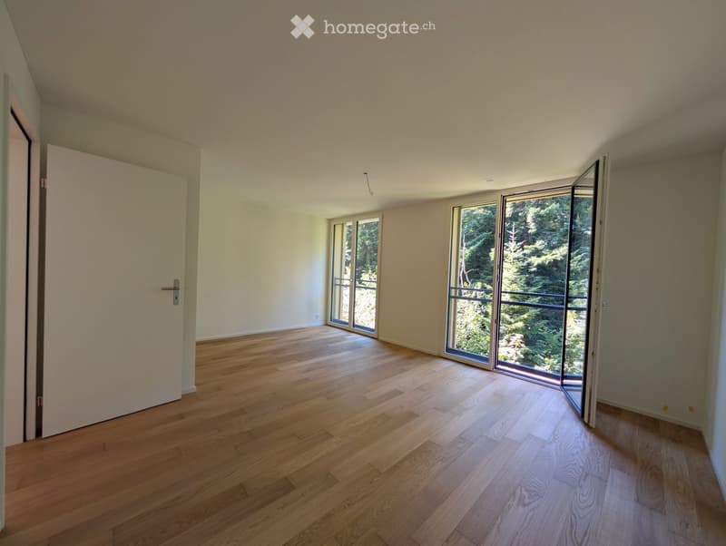 Empty room with wooden flooring, large windows, and sliding glass doors leading to a balcony.