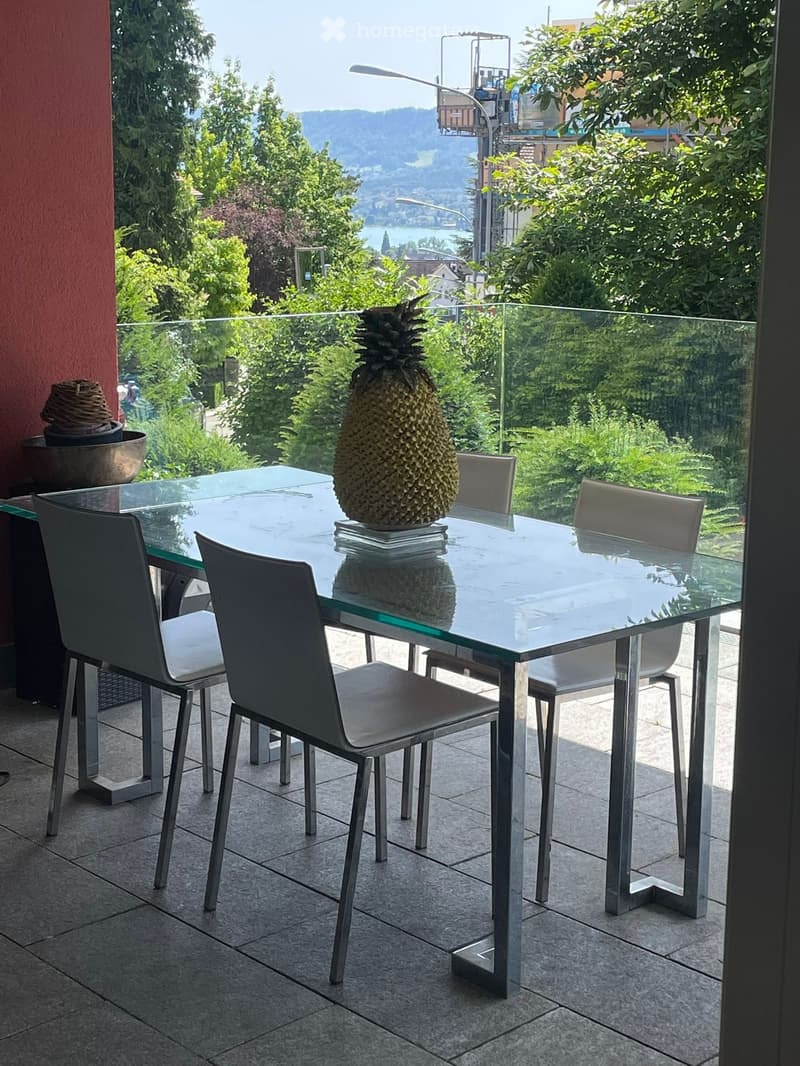 glass table, metal chairs, balcony, green glass railing, pineapple on the table, large windows overlooking the trees and mountains