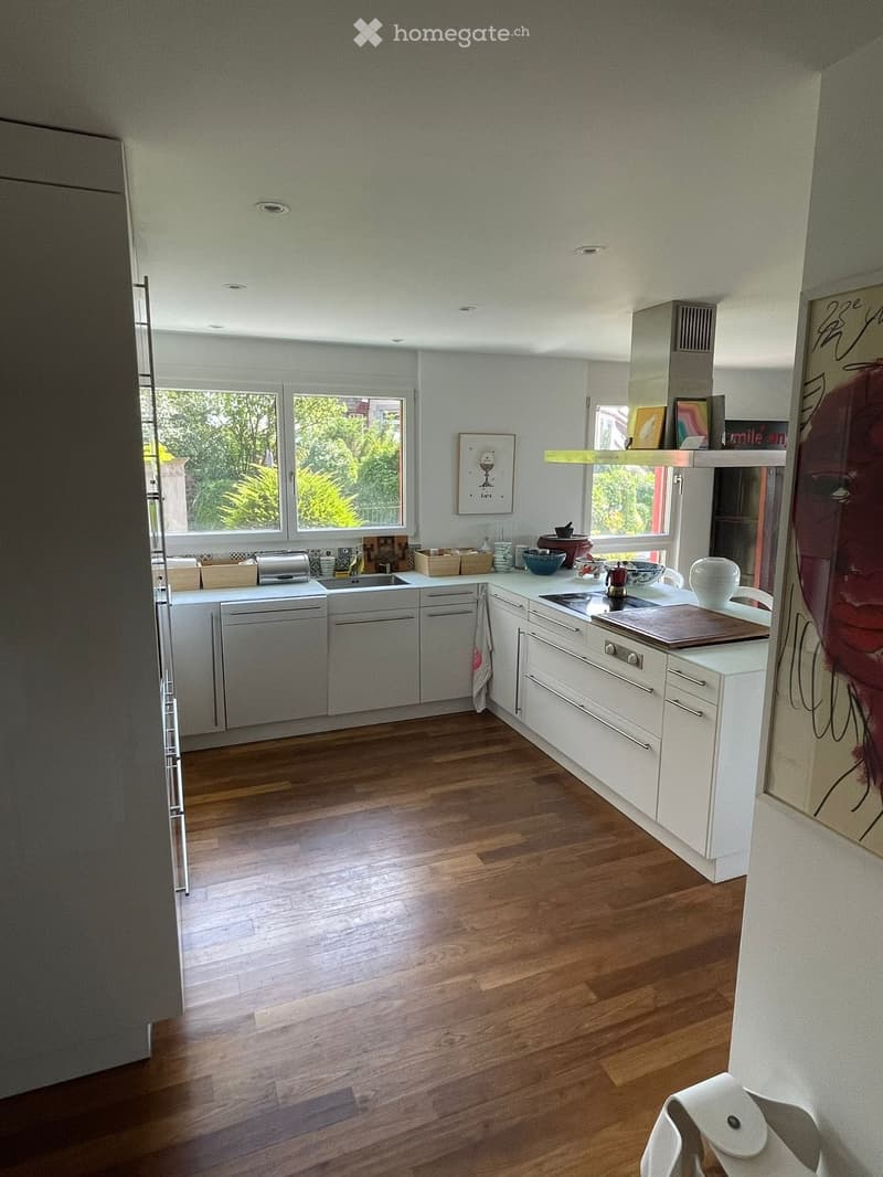 Modern kitchen with white cabinets, wooden floor, windows to the garden, large sink, cooking appliances, white artwork