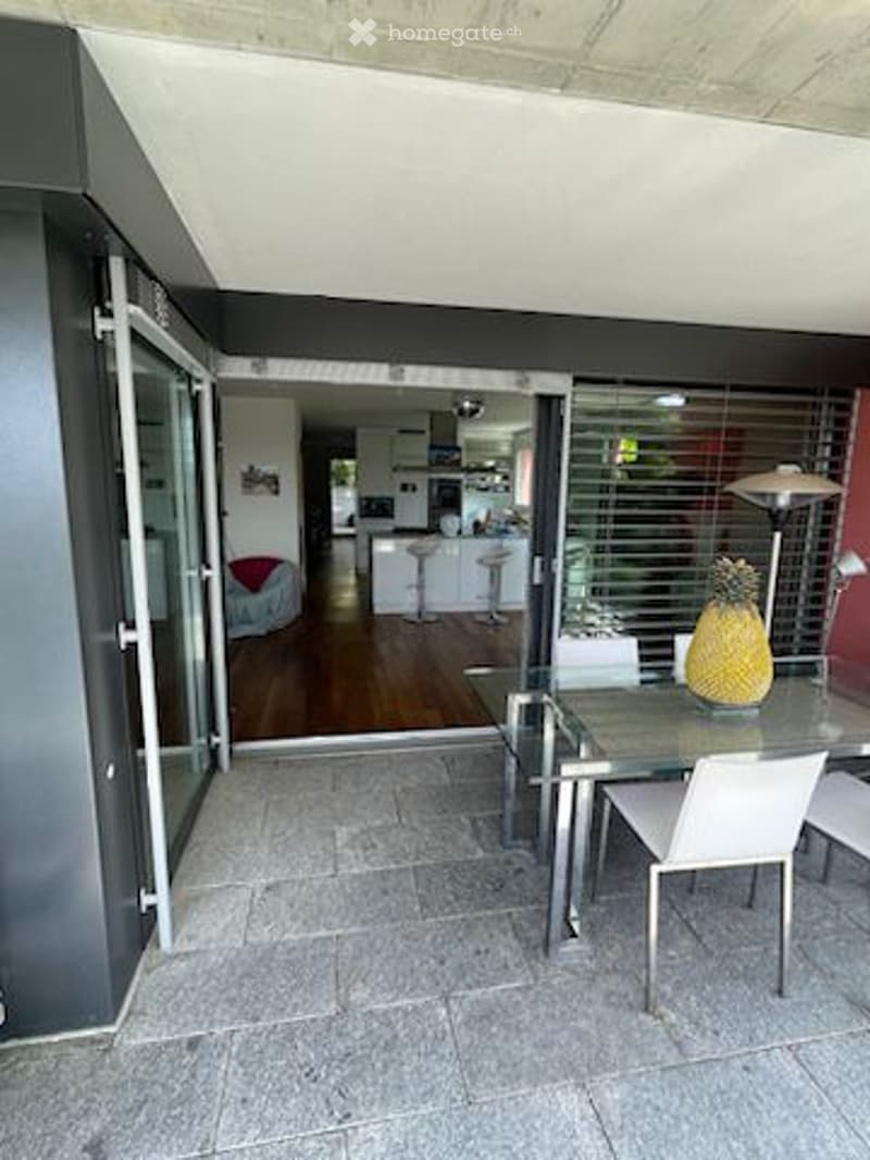 Balcony with dining table and chairs, open door leading to kitchen, wooden floor.