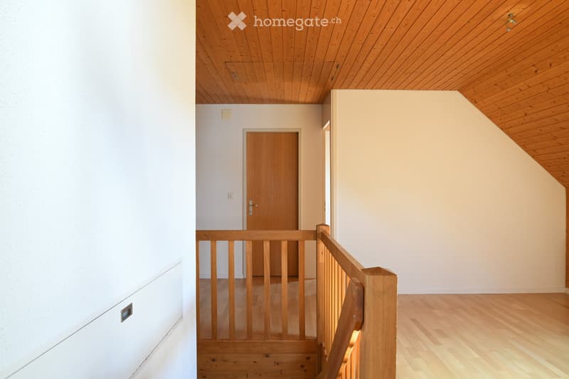 Staircase with wooden railings and a wooden door leading to another room. The walls are painted in neutral tones, and the ceiling is wooden.
