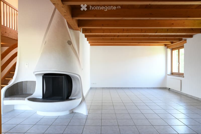 An unfurnished room with a modern, built-in fireplace, white walls, tiled floor, and wooden ceiling beams. A staircase is visible on the left side.