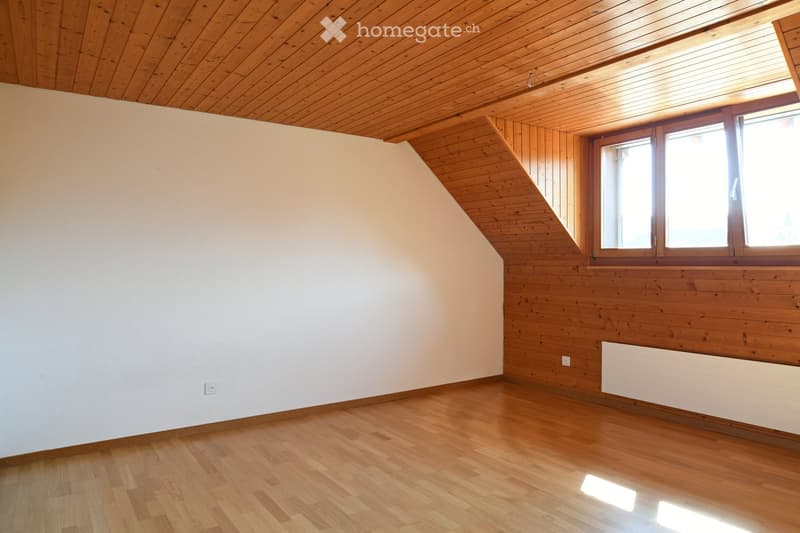 Empty room with wooden flooring, white walls, and wooden ceiling. Features large windows and a radiator on the right side.