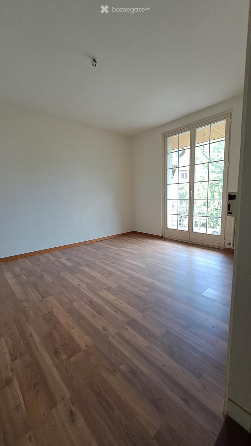 Empty room with wooden flooring and white walls, featuring a large sliding glass door leading to an outdoor area.