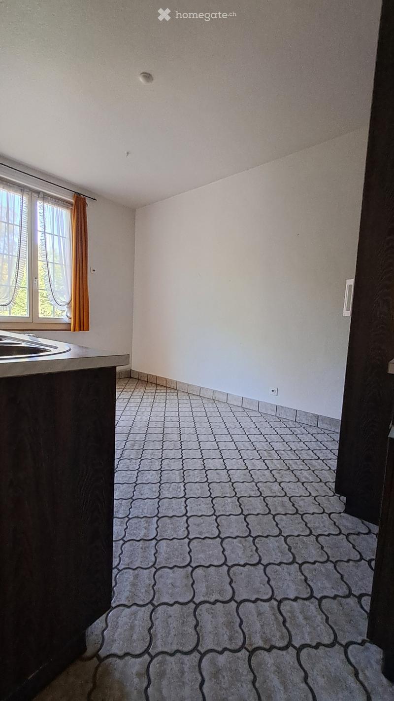 Empty room with white walls, grey tiled floor, and a window with orange curtains. No furniture or equipment present.
