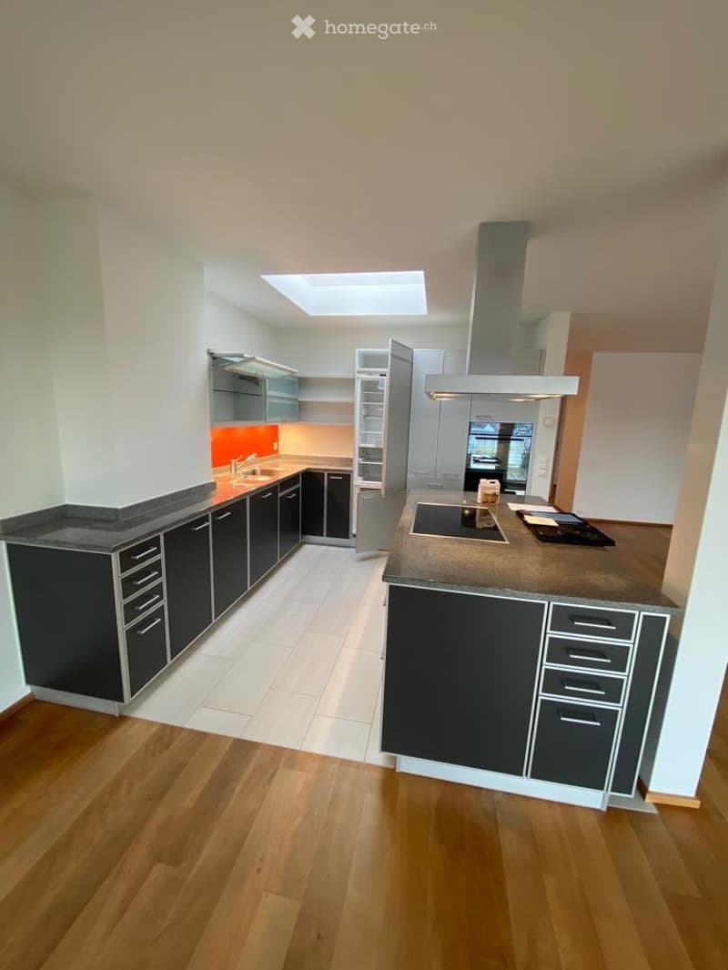 Modern kitchen with dark grey cabinets, light grey countertops, a central island, and a range hood. The space features a mix of wooden flooring and tiled areas, with built-in storage and a sleek design.
