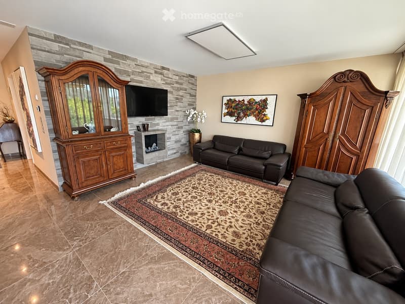 Elegant living room with dark leather sofas, a patterned rug, a wooden cabinet, a fireplace, and decorative artwork.