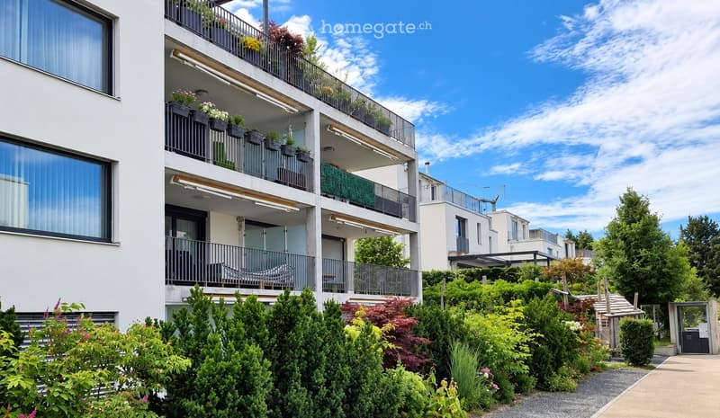 Modern multi-story apartment building with balconies, greenery, and potted plants.