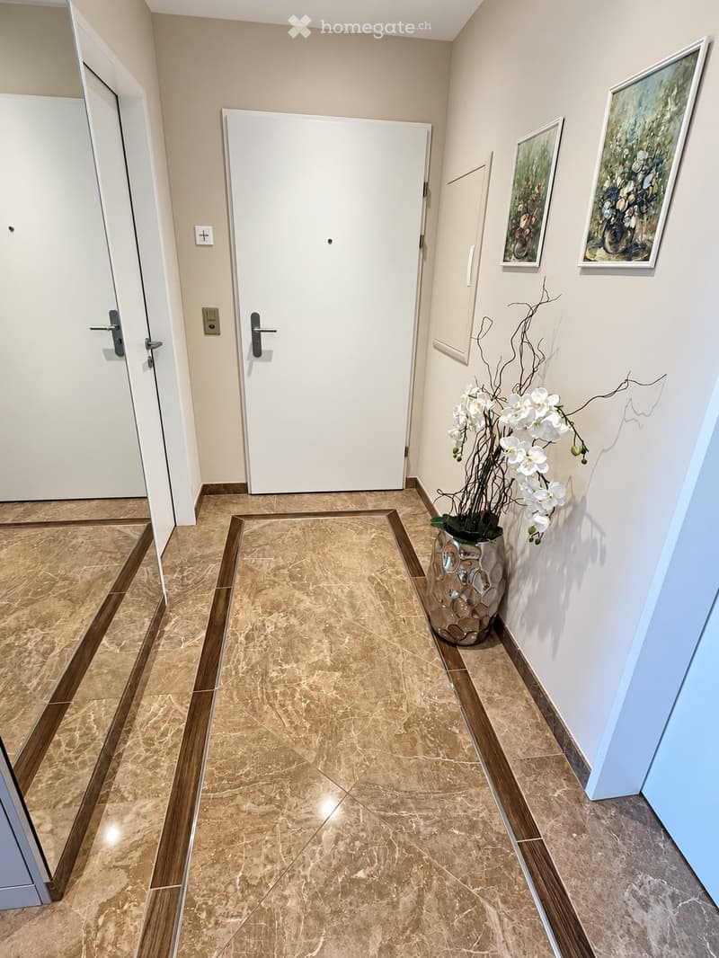 Clean hallway with beige tiled floor, white walls, two doors, and a decorative vase with white flowers on the right side.