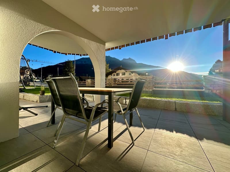 Balcony with a table and chairs, overlooking a scenic mountain view with the sun shining brightly.