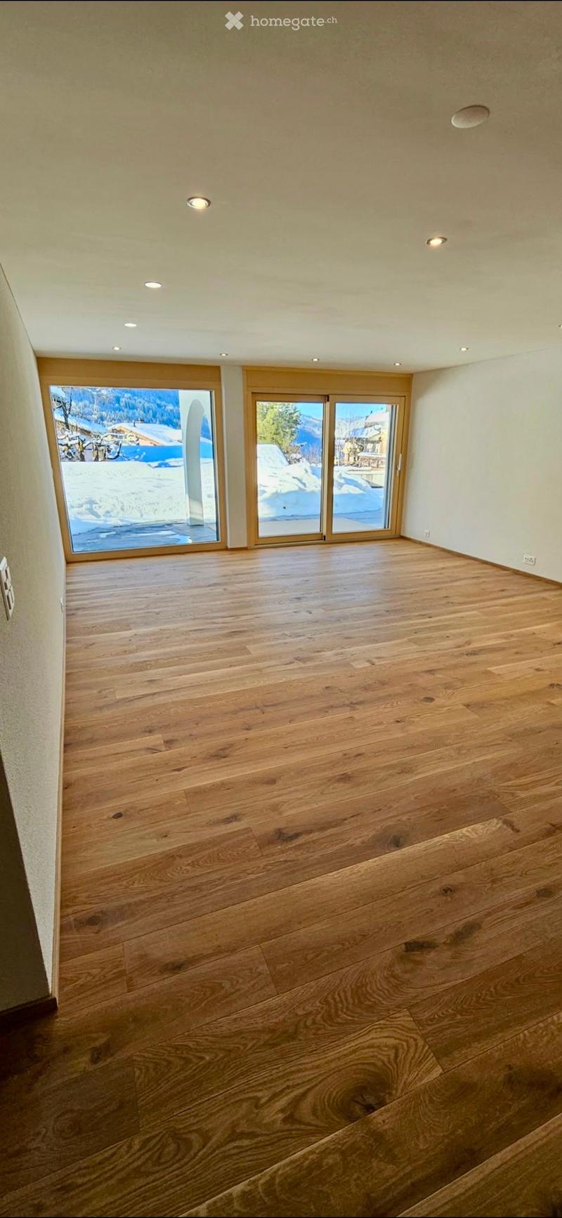 Empty room with wooden flooring, large windows, and recessed lighting. No furniture or equipment present.