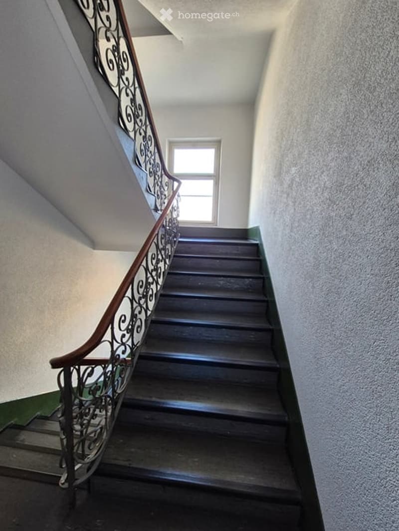 Wooden staircase with dark brown steps and a decorative wrought iron railing, leading up to a small window at the top.