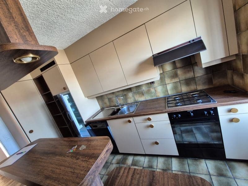 Modern kitchen with light-colored cabinets, wooden countertops, a sink, stove, oven, and a small wooden table.