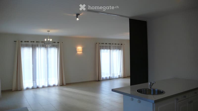 Empty room with tiled floor, large windows with curtains, and a kitchen counter with a sink.