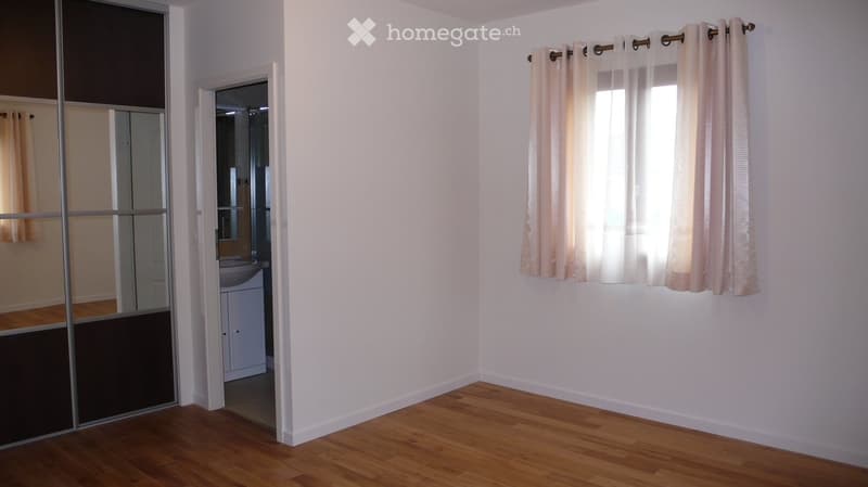 Empty room with wooden flooring, white walls, and a sliding glass door leading to a bathroom. Light pink curtains cover a window on the right side.