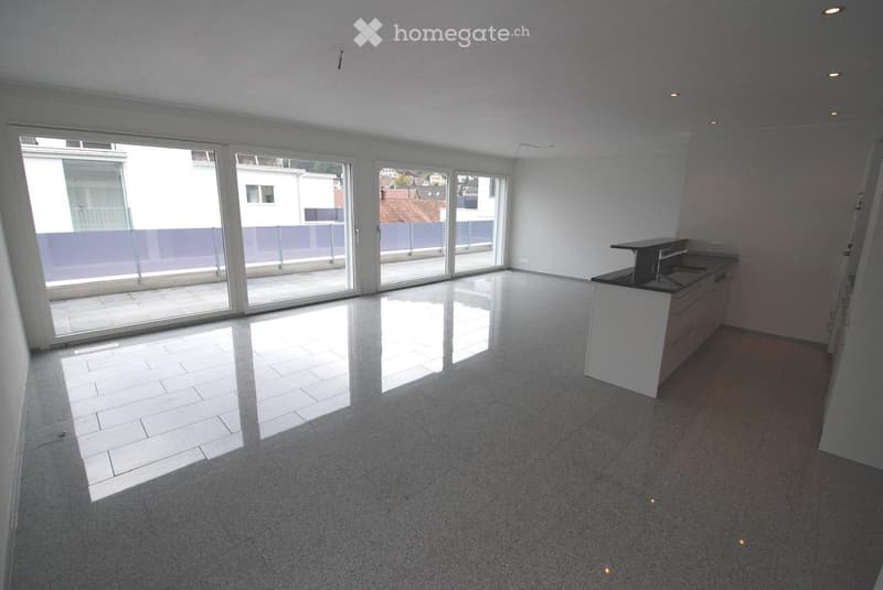 Empty room with large sliding glass doors leading to a balcony, white tiled floor, and a small kitchen counter with sink.