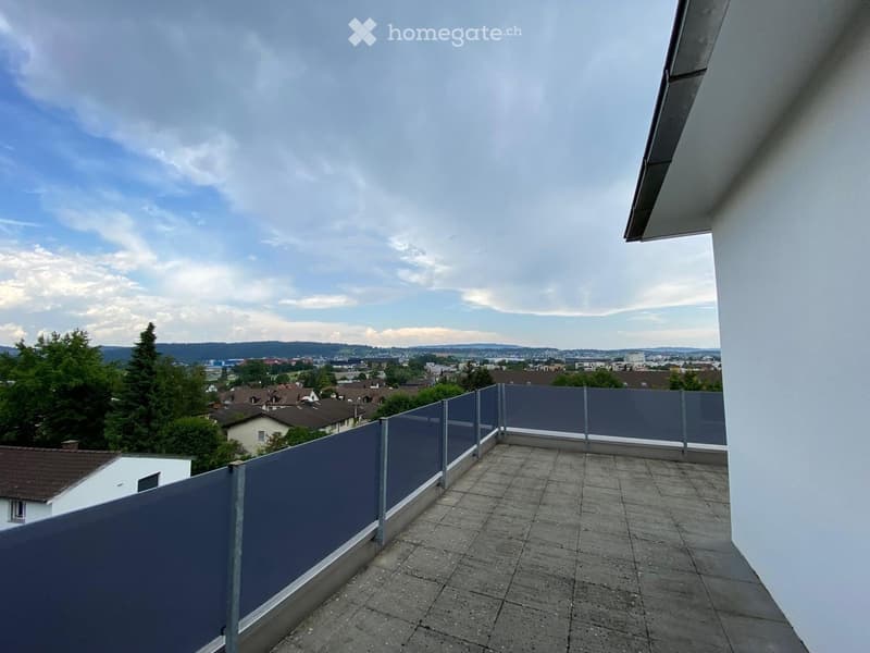 Balcony with grey tiled floor, grey metal railing, and a view of a town with houses and trees.