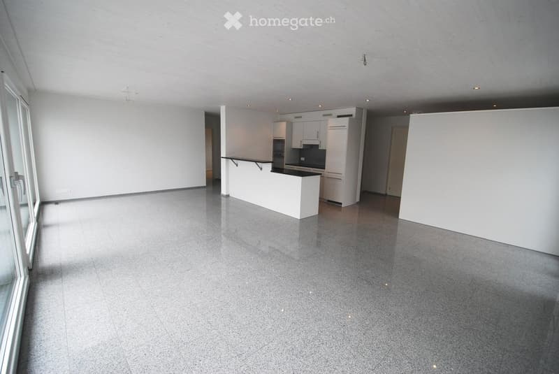Open-plan living and kitchen area with grey tiled flooring, white kitchen cabinets, and a central island.