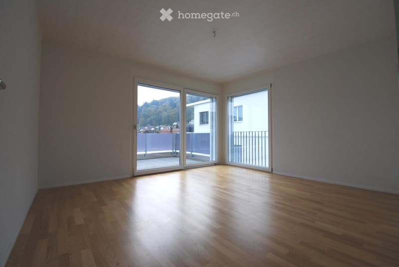 Empty room with wooden flooring and large sliding glass doors leading to a balcony. The walls are painted in a neutral tone, and the space is well-lit with natural light.