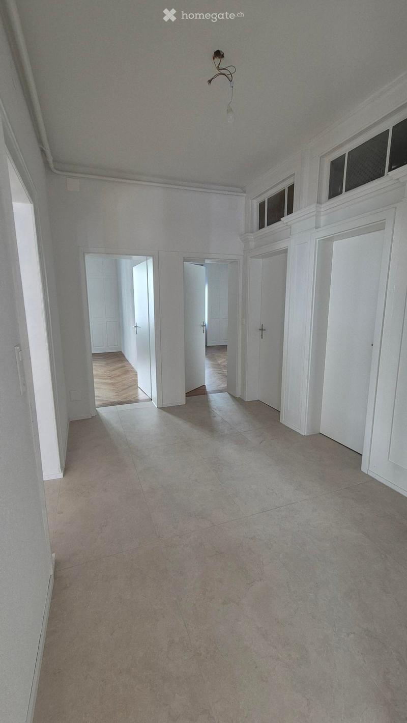Empty hallway with tiled floor, white walls, and several open doors leading to other rooms.
